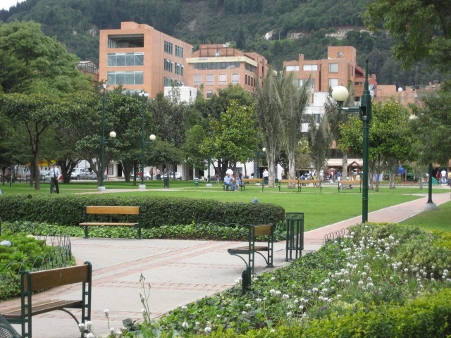 Tree-lined walkways and benches at Parque de la 93 in Bogotá with the eastern hills in the background.