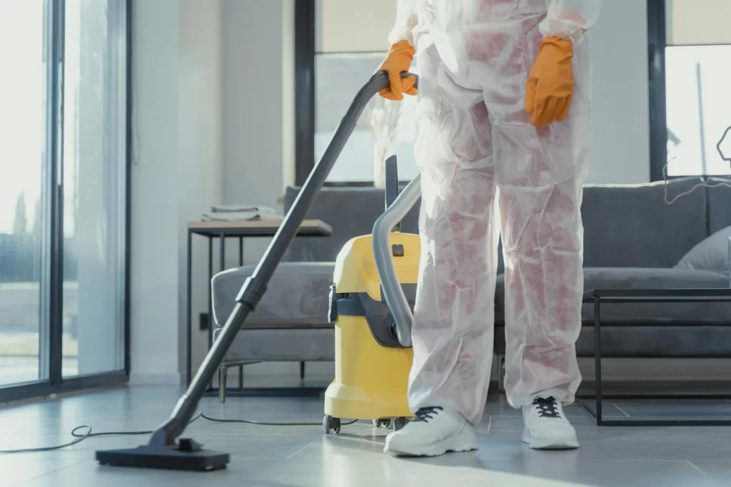 Cleaning staff in protective suit vacuuming living room in a luxury residence.