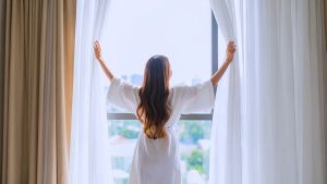 Mujer abriendo cortinas frente a una gran ventana con vista panorámica de la ciudad, representando penthouses de lujo en Bogotá