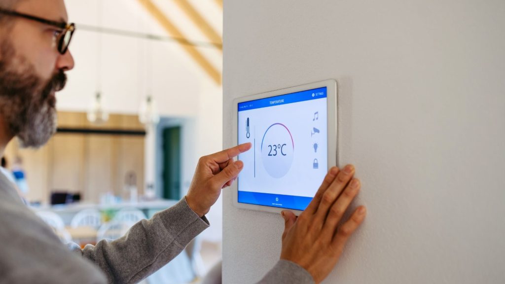 Hombre ajustando panel digital de control inteligente en una vivienda moderna.