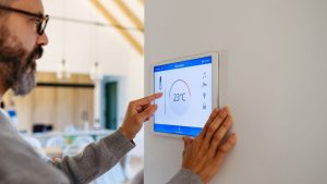 Hombre ajustando panel digital de control inteligente en una vivienda moderna.