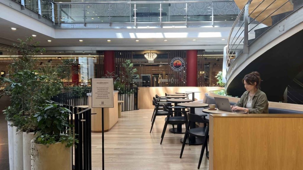 A digital nomad working on a laptop in a modern coworking space in Bogotá, featuring wooden decor and plants.