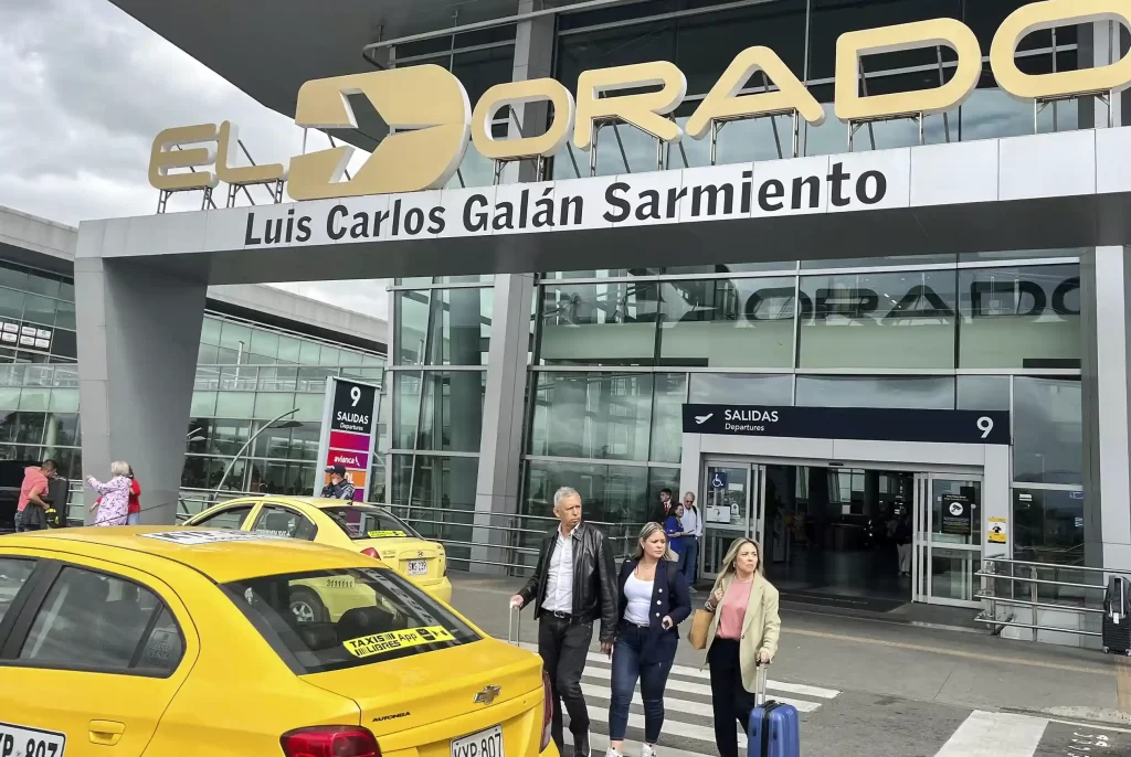 Zona de salidas del Aeropuerto El Dorado Luis Carlos Galán Sarmiento en Bogotá con viajeros de negocios y taxis disponibles en la vía.