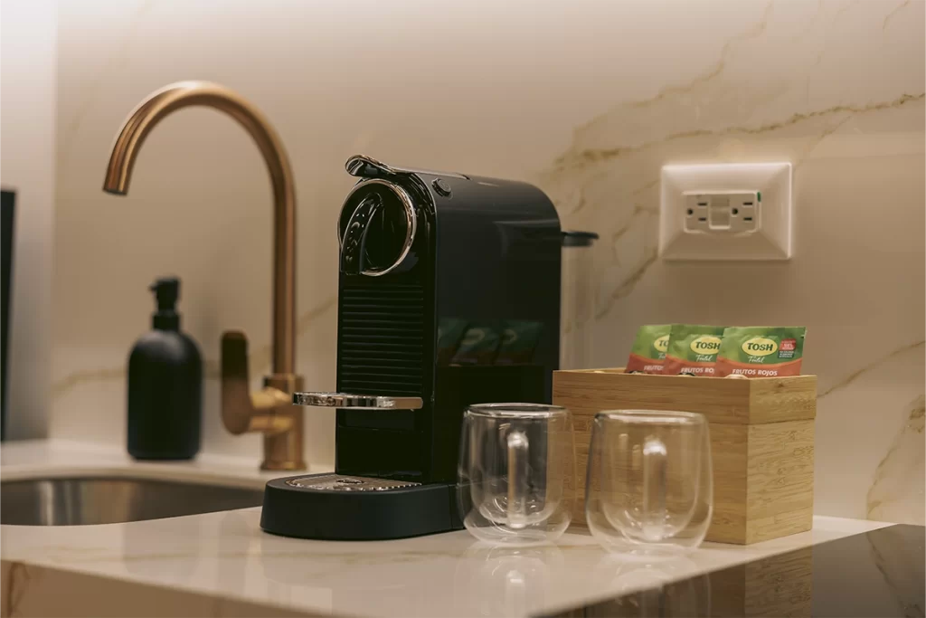 Cafetera Nespresso y vasos de vidrio sobre mesón de mármol con grifería dorada en Bogotá.