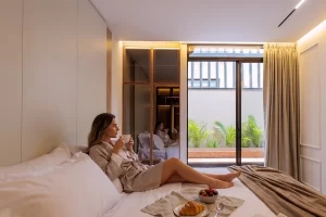 Persona en bata sobre cama con desayuno y vista a terraza con vegetación en Bogotá.
