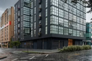 Edificio residencial moderno en Bogotá con calle mojada durante temporada de lluvias.