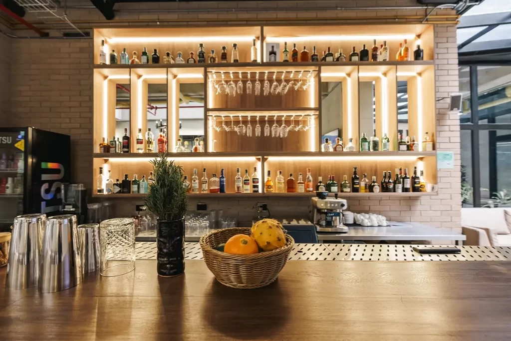 Barra de bar con estantes iluminados, botellas y frutas en el norte de Bogotá.