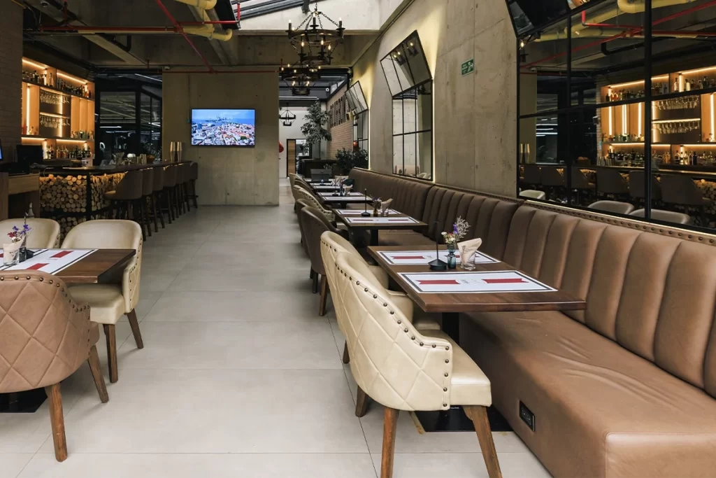 Salón de restaurante con banquetas de cuero, mesas servidas y techo industrial en Bogotá.