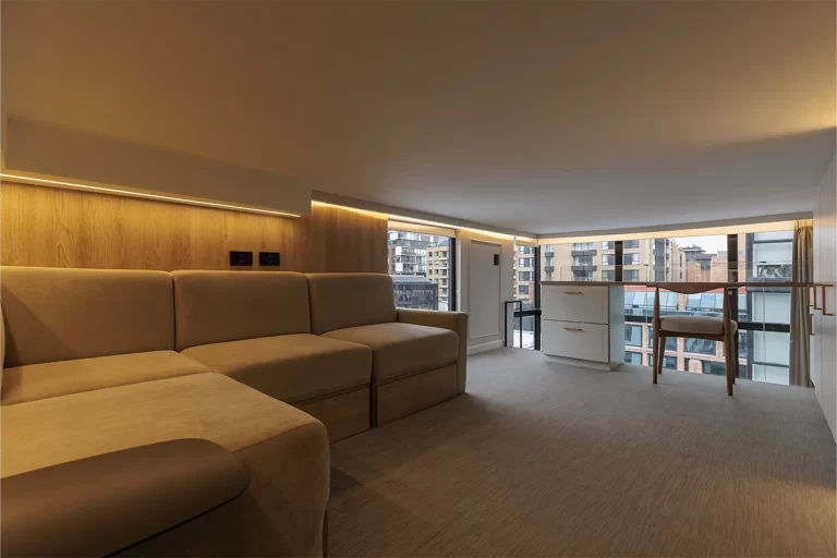 Sala de residencia con sofá modular, panel de madera iluminado y vista a Bogotá.