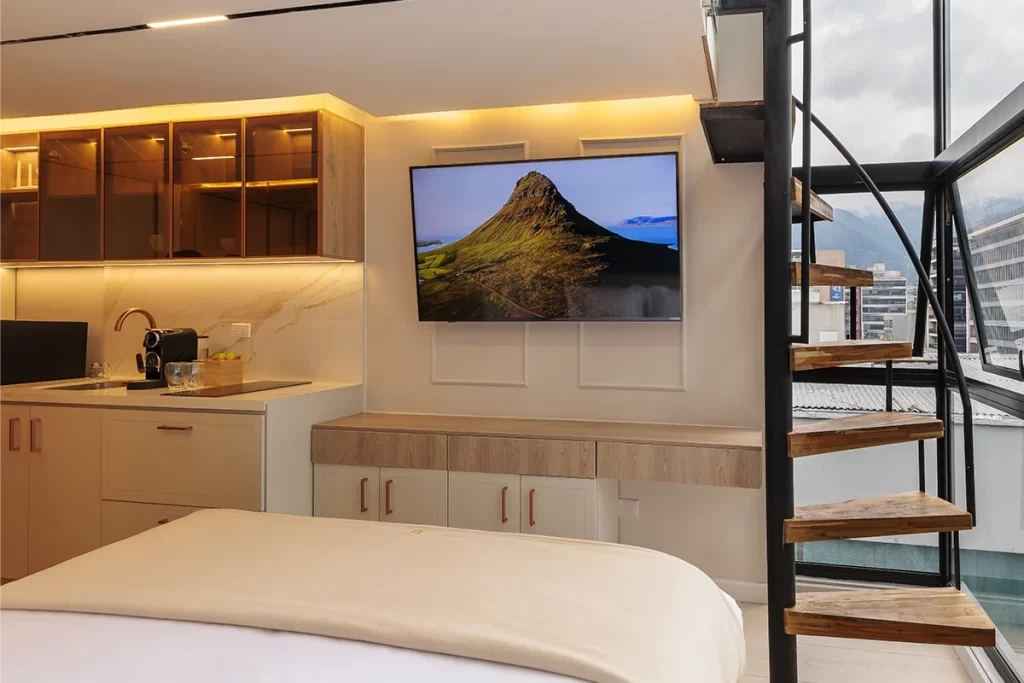 Loft con cama, cocina equipada, televisor y escalera de caracol con vista a Bogotá.